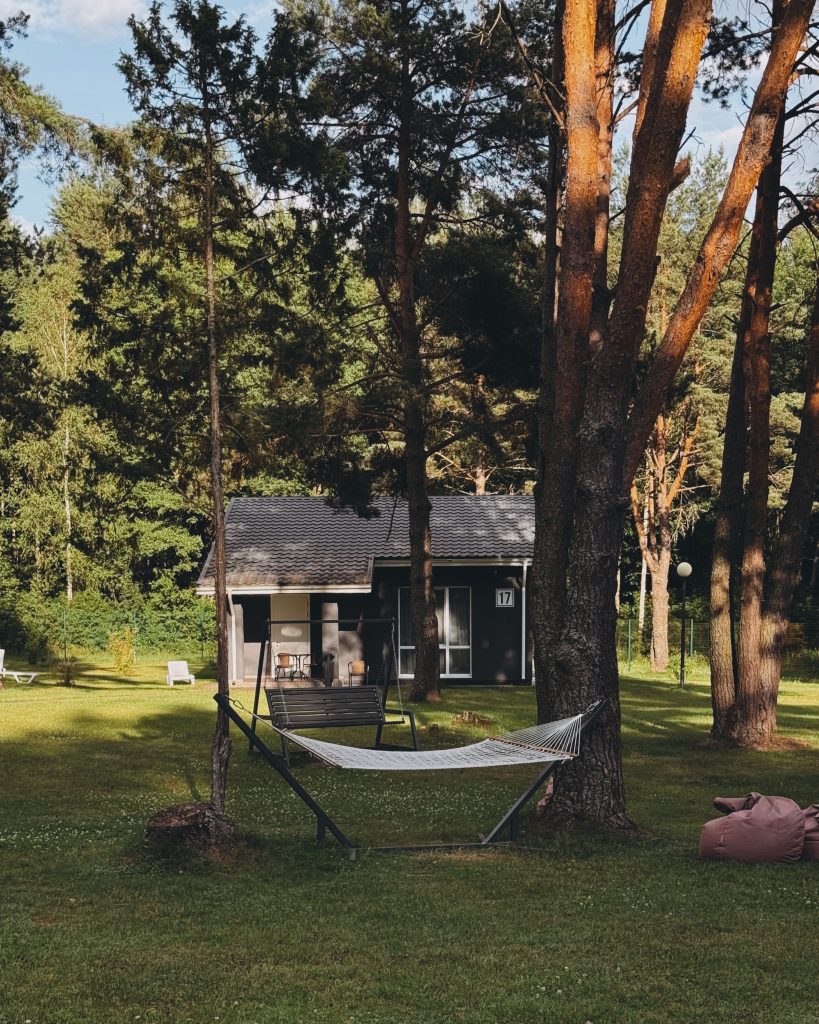 Serene forest scene with hammock under trees and modern cabin in the background.